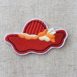 May include: Embroidered patch of a red sun hat with a black outline and white border. The hat features a detailed design with orange, yellow, and cream-coloured floral accents. The patch is designed for sewing or ironing onto fabric.