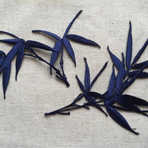 May include: Three dark blue embroidered bamboo leaf appliques on a beige fabric background.