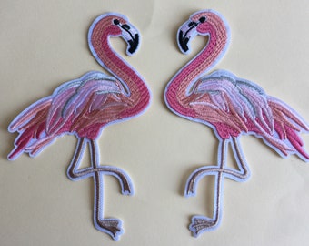 Könnte beinhalten: Zwei rosa Flamingo-Stickerei-Aufnäher zum Aufbügeln. Die Flamingos schauen sich mit gebogenem Hals an. Die Aufnäher sind auf weißem Hintergrund.