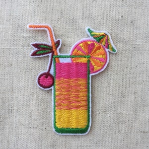 Könnte beinhalten: Gestickter Bügeleisen-Aufnäher mit einem rosa und gelben Cocktailgetränk mit einer Kirsche, einer Orangenscheibe und einem Strohhalm. Das Getränk befindet sich in einem hohen Glas mit grünem Rand.