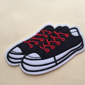 May include: Black and white embroidered patch of a pair of sneakers with red laces. The sneakers have a white sole and a black upper.