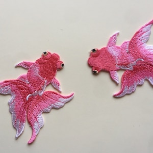 Puede incluir: Dos parches bordados de peces rojos rosas y blancos. Los peces rojos se miran y tienen ojos negros.