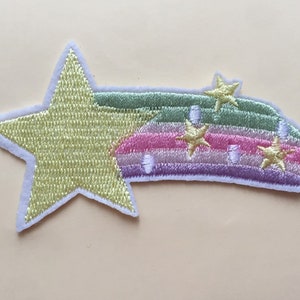 May include: Embroidered patch featuring a large yellow star and a rainbow with pink, green, and purple stripes. Small gold stars are embroidered on the rainbow. The patch has a white border.