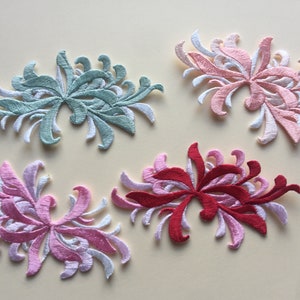 Könnte beinhalten: Vier gestickte Blumenapplikationen in verschiedenen Farben: Hellgrün, Rosa, Rot und Weiß. Die Applikationen haben die Form einer stilisierten Blume mit mehreren Blütenblättern.