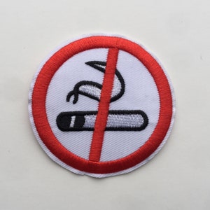 Könnte beinhalten: Ein rundes weißes Nichtraucherzeichen mit einem roten Kreis und einer diagonalen roten Linie durch eine schwarz-weiße Zigarettengrafik.