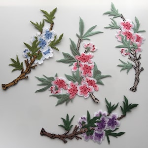 Peut inclure: Quatre patchs de fleurs brodés avec des feuilles vertes et des tiges brunes. Les patchs présentent des fleurs roses, violettes et bleues.