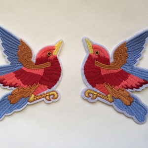 Puede incluir: Dos parches bordados para planchar de pájaros rojos, naranja y azules con las alas extendidas.