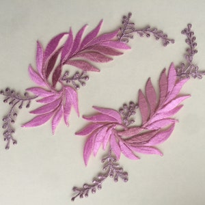 Könnte beinhalten: Zwei rosa bestickte Blumenapplikationen mit einem Blattdesign. Die Applikationen sind perfekt, um Kleidung, Kunsthandwerk oder Wohnaccessoires einen Hauch von Eleganz zu verleihen.