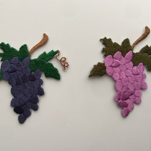 Pode incluir: Dois patches bordados para passar a ferro com forma de uvas. Um patch é roxo e o outro é rosa.