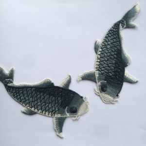 Könnte beinhalten: Zwei gestickte Bügelbilder von schwarzen und weißen Koi-Fischen. Die Fische sind in entgegengesetzte Richtungen gerichtet.