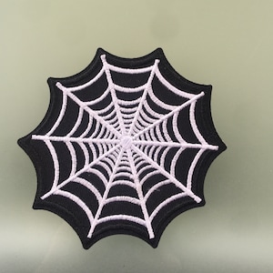 Pode incluir: Um remendo bordado de teia de aranha em preto e branco. A teia é branca e o fundo é preto.