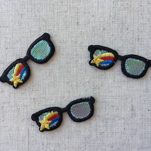 May include: Three black and white embroidered iron-on patches of sunglasses with a rainbow design in the lenses.