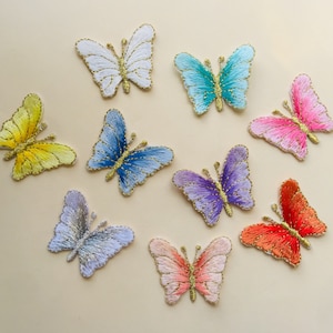 May include: Assortment of ten embroidered iron-on patches featuring butterflies in various colours, including yellow, blue, purple, pink, red, and white. Each butterfly has gold glitter accents.