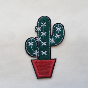 May include: Green embroidered cactus with white flowers in a red pot.