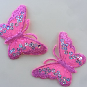 May include: Two pink butterfly-shaped fabric patches with iridescent sequins. The butterflies have a delicate, embroidered design.