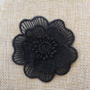 Puede incluir: Aplique de flor de encaje negro con un diseño delicado. La flor está hecha de encaje negro y tiene un centro elevado. Es perfecta para añadir un toque de elegancia a cualquier proyecto.