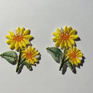 May include: Two embroidered yellow sunflower patches with green leaves. The sunflowers have white centres and yellow petals.