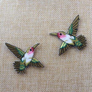 May include: Two green and white embroidered hummingbird patches with pink accents. The hummingbirds are facing opposite directions.
