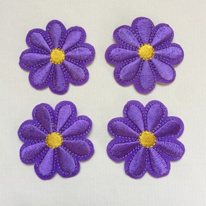 Puede incluir: Cuatro parches de flores de fieltro morado con centros amarillos. Las flores tienen ocho pétalos cada una.
