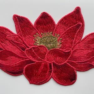 Peut inclure: Une fleur de lotus rouge brodée avec un centre doré. La fleur est un patch ou une applique décorative.