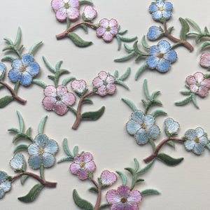 May include: Assortment of embroidered flower patches in pink and blue shades. The patches feature delicate floral designs with intricate details.