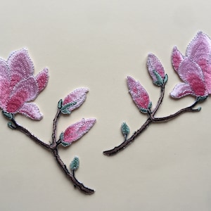 Könnte beinhalten: Zwei gestickte rosa Magnolienblüten-Patches mit grünen Stielen und Blättern.