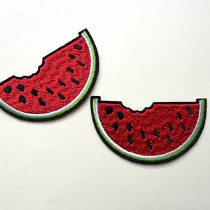May include: Two embroidered watermelon slice patches. Each patch features a red interior with black seeds, a green rind, and a white border. One slice has a bite taken out of it. These patches are ideal for adding a fun, summery touch to clothing or accessories.