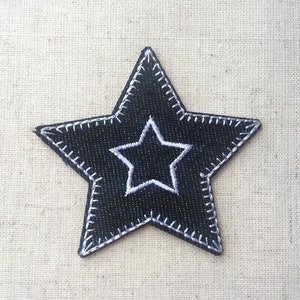 May include: A black star-shaped patch with a white star in the centre. The star is outlined in white and has a stitched edge.