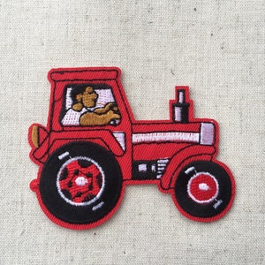 Peut inclure: Tracteur jouet rouge avec un conducteur noir et des roues blanches. Le tracteur a une bande blanche sur le capot et un tuyau d'échappement noir.