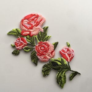 以下が含まれることがあります： ピンクと赤のバラが緑の葉で囲まれた刺繍パッチ。バラは様々なサイズで、繊細なヴィンテージスタイルです。
