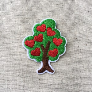 Pode incluir: Um remendo bordado que representa uma árvore com um tronco marrom e folhas em forma de coração vermelho.