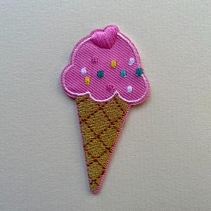 Puede incluir: Parche bordado de cono de helado. La bola de helado rosa tiene chispas de colores y un detalle de corazón. El cono es de color marrón dorado con un patrón de diamantes. Adecuado para ropa o accesorios.