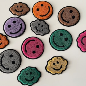 May include: Assortment of 11 colourful embroidered smiley face patches in various shapes, including clouds and circles. The patches are made of fuzzy yarn and have black embroidered details.