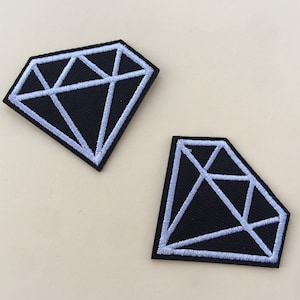 May include: Two black diamond-shaped patches with white outlines. The patches are made of fabric and have a stitched design.