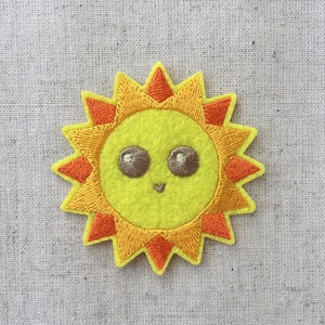 May include: A yellow felt sun with orange rays and a smiling face with brown eyes.
