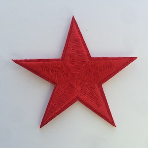 Peut inclure: Un écusson en forme d'étoile rouge brodée. L'étoile est à cinq branches et a une surface légèrement texturée.
