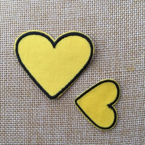 May include: Two yellow felt heart-shaped patches with black outlines. The larger heart is on the left and the smaller heart is on the right.