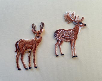 以下が含まれることがあります： 2つの刺繍された鹿のパッチ。1つは角があり、もう1つはより手の込んだ角のデザインです。どちらのパッチも茶色で、白いアクセントと黒い蹄があり、ニュートラルな背景に配置されています。