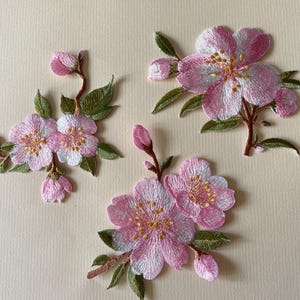 Peut inclure: Écussons floraux brodés représentant des fleurs de cerisier roses et blanches avec des feuilles vertes et des tiges marron. Les écussons comprennent des fleurs écloses et des bourgeons, parfaits pour embellir des vêtements ou des accessoires.