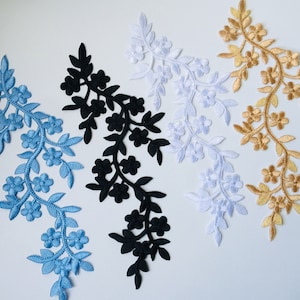 Könnte beinhalten: Fünf florale Stickerei-Patches in verschiedenen Farben: Blau, Schwarz, Weiß und Gold. Jeder Patch zeigt eine zarte Ranken mit kleinen Blüten.