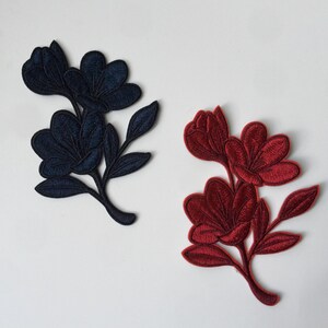 Könnte beinhalten: Zwei gestickte Stoffblumen-Applikationen. Eine ist marineblau und die andere ist burgunderrot.