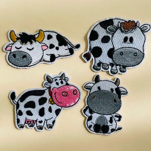 Puede incluir: Cuatro parches bordados para planchar que representan vacas de dibujos animados en varias poses. Las vacas son blancas con manchas negras y tienen ojos y narices negros. Los parches son perfectos para añadir un toque caprichoso a la ropa, los bolsos u otros artículos de tela.