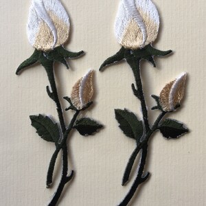 May include: Two white and beige embroidered rosebud patches with green stems and leaves.