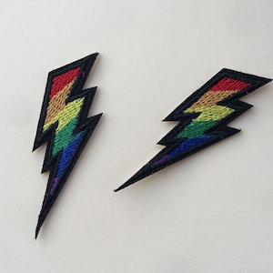 May include: Two iron-on patches shaped like lightning bolts, with rainbow coloured embroidery. The patches are black.