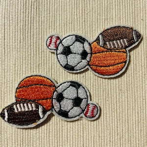 Può includere: Toppe ricamate da stirare con diverse palle da sport, tra cui una palla da basket, una palla da football americano, una palla da baseball e una palla da calcio. Le toppe sono bianche, marroni, arancioni e nere.