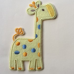 May include: A yellow felt giraffe applique with blue and orange spots. The giraffe has a yellow mane and a brown eye.