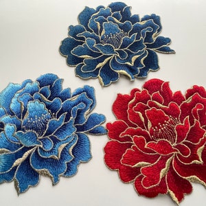 以下が含まれることがあります： 3つの刺繍された布の花のパッチ。1つは青、1つは赤、もう1つは濃い青。すべて金色の刺繍のディテールがあります。