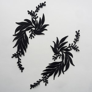 Puede incluir: Dos apliques de tela negra en forma de ramas con hojas. Las ramas están curvadas y tienen pequeños capullos de flores.