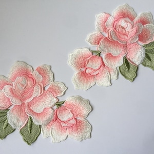 May include: Two embroidered pink and white flower patches with green leaves. The flowers are in a delicate floral design.
