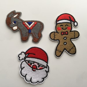 May include: Three embroidered iron-on patches featuring a gingerbread man, a donkey, and Santa Claus. The gingerbread man is brown with a red hat and a white bow tie. The donkey is gray with a red, white, and blue saddle. Santa Claus is wearing a red hat and a white beard.